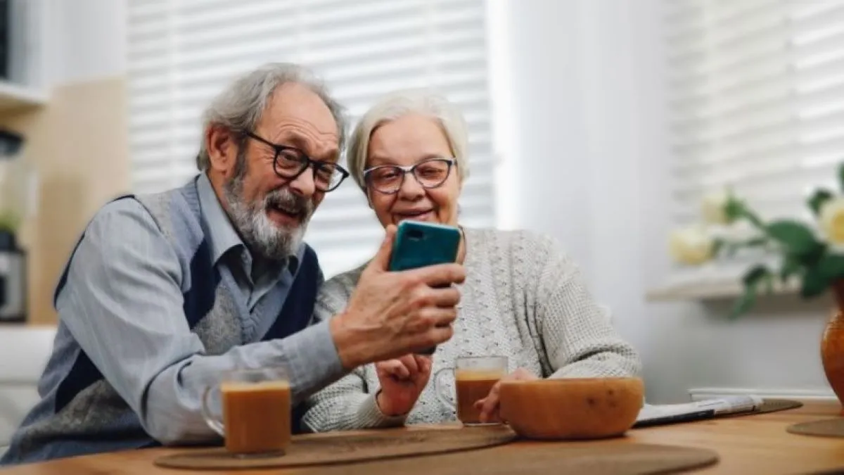 Casal de idosos olha no celular, como se estivessem lendo versículos de reflexão bíblica para a terceira idade
